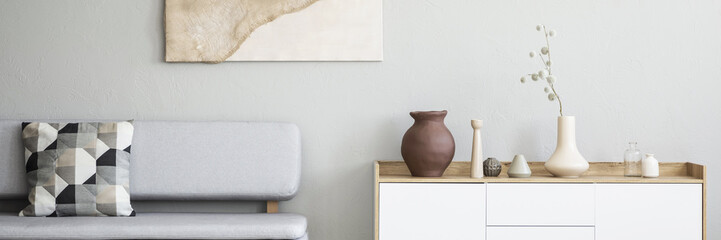 Graphic, pattern pillows on a gray sofa and a white, wooden cabinet with vases in a monochromatic living room interior with natural decorations