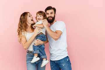 Wall Mural - A happy family on pink studio background. The father, mother and son posing together