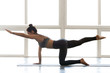 Young sporty attractive woman practicing yoga, doing Donkey Kick exercise, Bird dog pose, working out, wearing sportswear, grey pants, top, indoor full length, at yoga studio