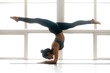 © fizkes - Young yogi attractive woman practicing yoga, doing Pincha Mayurasana exercise, handstand pose, working out, wearing sportswear, grey pants, top, indoor full length, at yoga studio, side view