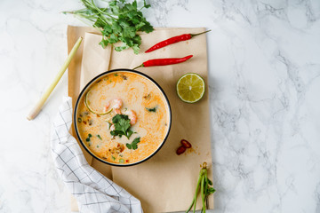 Tom yum soup with shrimps, traditional thai spicy dish served with cilantro and lime slices on marble table. Top view with copy space