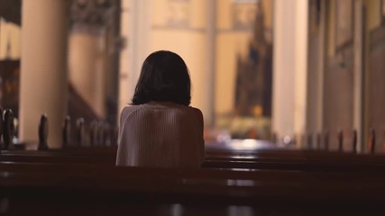 Wall Mural - Back view of a young Christian woman sitting in the church while praying to the GOD. Shot in 4k resolution