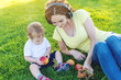 © Artem - Young modern mom in headphones playing in a green meadow with her cute baby son in a Sunny Park. Joy of motherhood