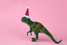 Funny Green Dinosaur Toy In Little Santa Claus Hat  On Pastel Pink Background