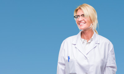 Wall Mural - Middle age blonde therapist woman wearing white coat over isolated background looking away to side with smile on face, natural expression. Laughing confident.