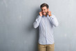© Krakenimages.com - Handsome young business man over grey grunge wall wearing elegant shirt covering ears with fingers with annoyed expression for the noise of loud music. Deaf concept.