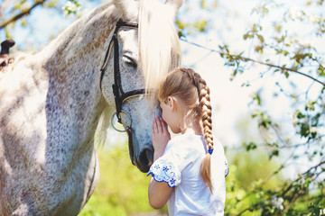 Cute little girl whith white horse in blooming apple orchard