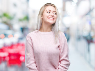 Young blonde woman wearing winter sweater over isolated background looking away to side with smile on face, natural expression. Laughing confident.