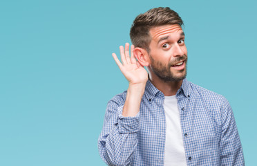 Young handsome man wearing white t-shirt over isolated background smiling with hand over ear listening an hearing to rumor or gossip. Deafness concept.