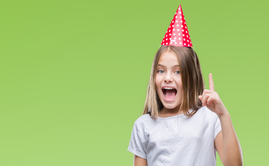 Young beautiful girl wearing birthday cap over isolated background pointing finger up with successful idea. Exited and happy. Number one.