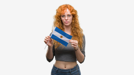 Canvas Print - Young redhead woman holding flag of Argentina with a confident expression on smart face thinking serious