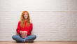 © Krakenimages.com - Young redhead woman sitting over brick wall eating popcorn screaming proud and celebrating victory and success very excited, cheering emotion