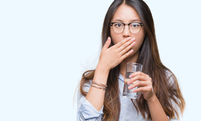 Canvas Print - Young asian woman drinking a glass of water over isolated background cover mouth with hand shocked with shame for mistake, expression of fear, scared in silence, secret concept