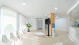 Fototapeta Londyn - Panorama of a bright reception and waiting room in a clinic with desk, modern chairs and plants. Indoor mockup with screen with copy space.