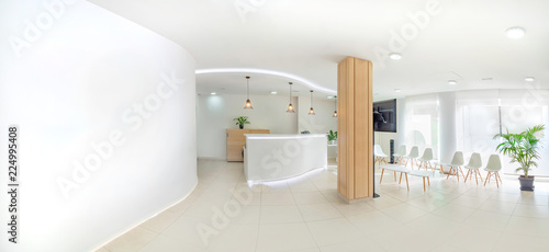 Fotomural Panorama of a bright reception and waiting room in a clinic with desk, modern chairs and plants