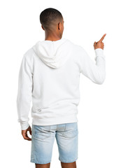 Dark-skinned young man with white sweatshirt pointing back with the index finger on isolated white background