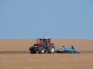 Wall Mural - Red tractor with plow on the field. Tractor on the field. Summer field and red tractor.