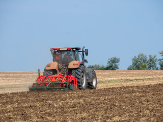 Red tractor with plow on the field. Tractor on the field. Summer field and red tractor.