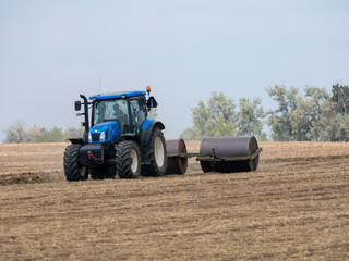 Wall Mural - Tractor pulls rollers on the field. Blue Tractor with rollers on the field. Tractor on summer field.