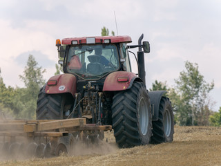 Wall Mural - Red tractor with plow on harvest field. Summer field and red tractor. Tractor on harvest field. Lowing after harvest. Plowing on the field.