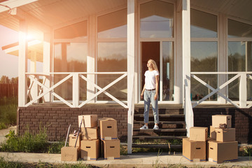 Blonde woman moved in new light house. Girl waiting movers to move boxes in home