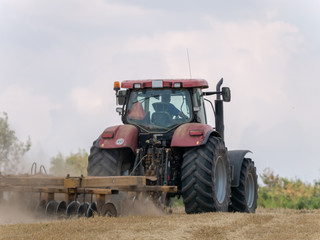 Wall Mural - Red tractor with plow on harvest field. Summer field and red tractor. Tractor on harvest field. Lowing after harvest. Plowing on the field.