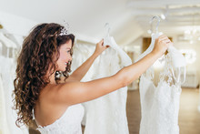 Attractive Young Brunette Woman Is Smiling And Enjoying While Choosing Wedding Dress In Modern Wedding Salon.