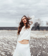 Young pretty brown-haired woman standing in the field with wheat