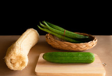 Luffa Cylindrica (L.) M.J.Roem And Trichosanthes Anguia Linn. Green Fresh On Chopping Board With Basket Weave And Dry Sponge Gourd. Black Background And Shadow.