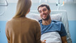 © Gorodenkoff - In the Hospital, Man Recovering from Illness Lying in Bed, Loving Wife Visits Him. He is Smiling and Looking at Wife.