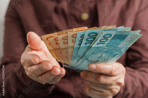 Brazilian currency. Front view of old woman\'s hand handling bills.
