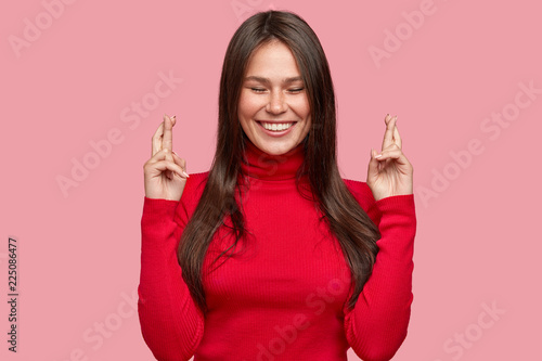 Photographie Indoor shot of cheerful brunette girl with satisfied expression, keeps fingers i