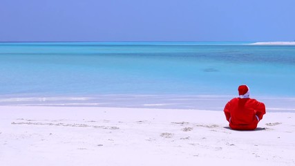 Wall Mural - Man in Santa Claus Hat sitting on sandy beach