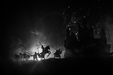 Medieval battle scene with cavalry and infantry. Silhouettes of figures as separate objects, fight between warriors on dark toned foggy background with medieval castle. Night scene. Selective focus