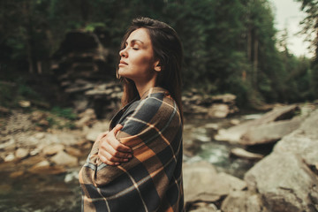 Wall Mural - Pleasant thoughtful woman covering herself with a warm blanket and standing in the forest