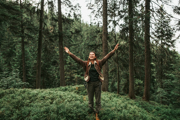 Wall Mural - I am happy and free. Full length portrait of spirited young lady with closed eyes enjoying travel in the woods. She is spreading arms with joy and smiling