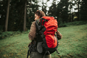 Wall Mural - Brave traveler. Back view of charming girl with backpack walking alone in green meadow