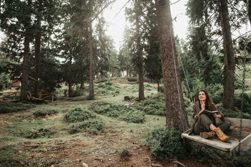 Wall Mural - Peace and quiet. Portrait of beautiful young woman searching inspiration in forest. She is touching chin with pen and looking away with smile