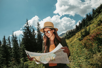 Wall Mural - Where should i go. Waist up portrait of smiling girl in sunglasses searching right direction on location map. Beautiful sky with clouds, green trees and plants on background