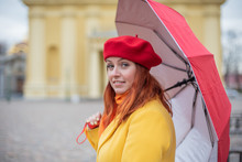 A Sad Young Woman In Colorful, Warm Clothes With A Red Umbrella Sits Alone On A Bench. A Girl Sits On A Bench In A Yellow Coat And An Umbrella In The Autumn.