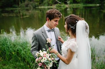 Wall Mural - Portrait of an attractive groom looking bride on nature in the park. Wedding ceremony near lake. Happy and joyful moment.