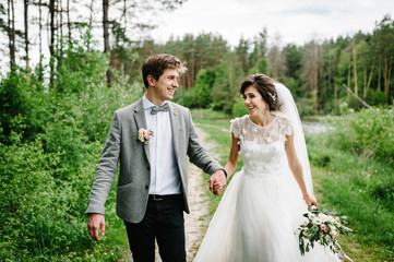 Wall Mural - Romantic couple newlyweds, bride and groom is walking on a trail in an green park. Happy and joyful wedding moment.