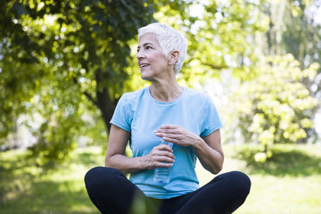 Wall Mural - Senior woman rests and drinks water after workout