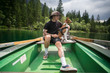 © BublikHaus - Young man in hiking camping outfit sits together with his puppy pet, basenji breed dog on rowing boat, swimming in alpine mountain lake, enjoys healthy active lifestyle