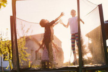 Cheerful happy kids having fun and jumping in a trampoline on a sunny day. Happy childhood.