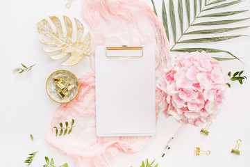 Wall Mural - Modern home office desk workspace with blank paper clipboard, pink hydrangea flowers bouquet, tropical palm leaf, pastel blanket, monstera leaf plate and accessories on white background. Flatlay.