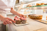 Women putting muffins on display in bakery shop, close-up