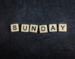 Scrabble letter tiles on black slate background spelling Sunday