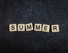 Scrabble letter tiles on black slate background spelling Summer