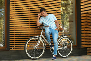 Wall Mural - Handsome young hipster man with bicycle near wooden wall outdoors